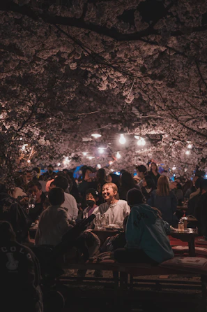 A lively outdoor event with people chatting under blooming cherry blossom trees in soft spring light