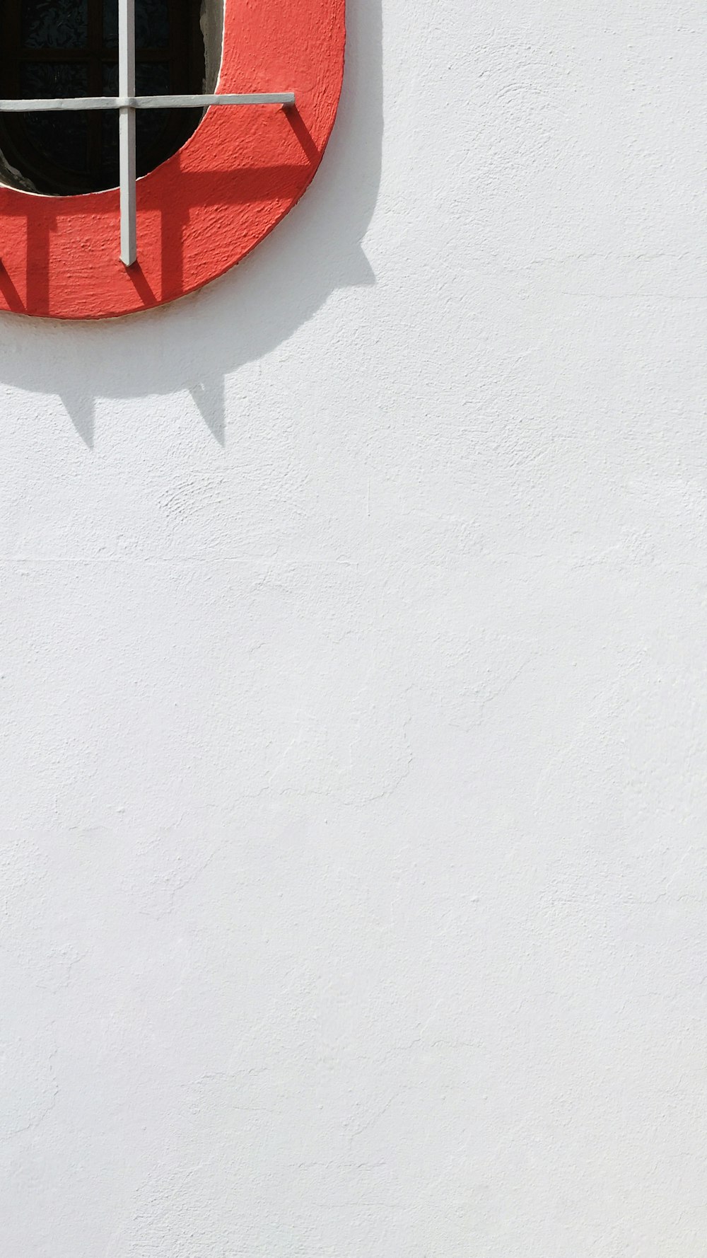a white wall with a red window and a cross on it
