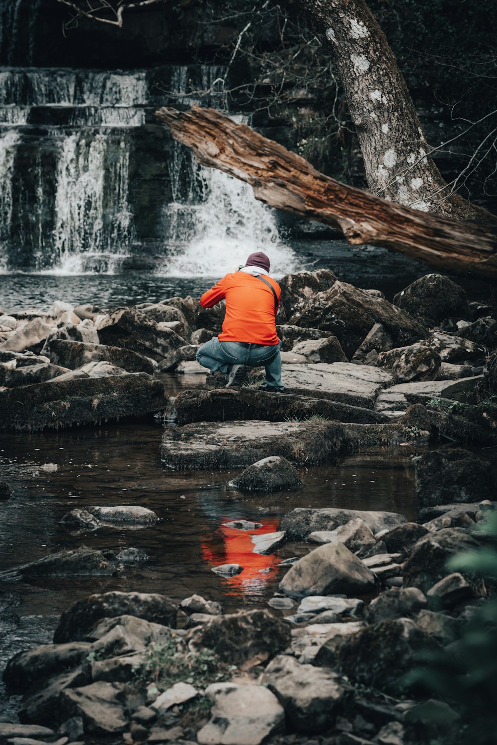 a man kneeling on a rock in front of a waterfall