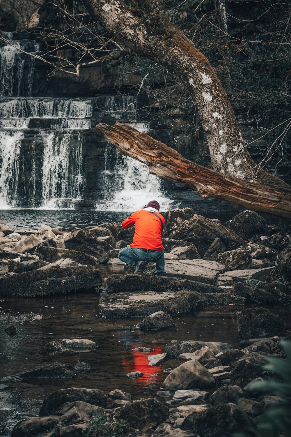 Un homme en veste orange debout sur des rochers près d’une cascade