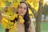 a woman standing under a tree with yellow leaves