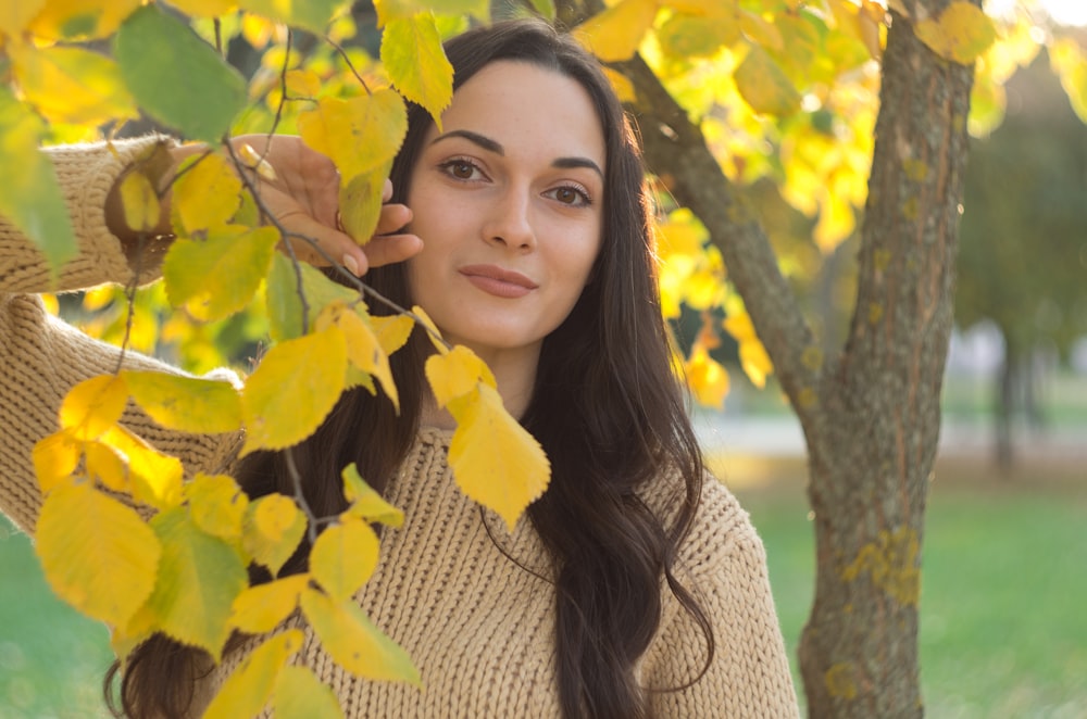 a woman standing under a tree with yellow leaves