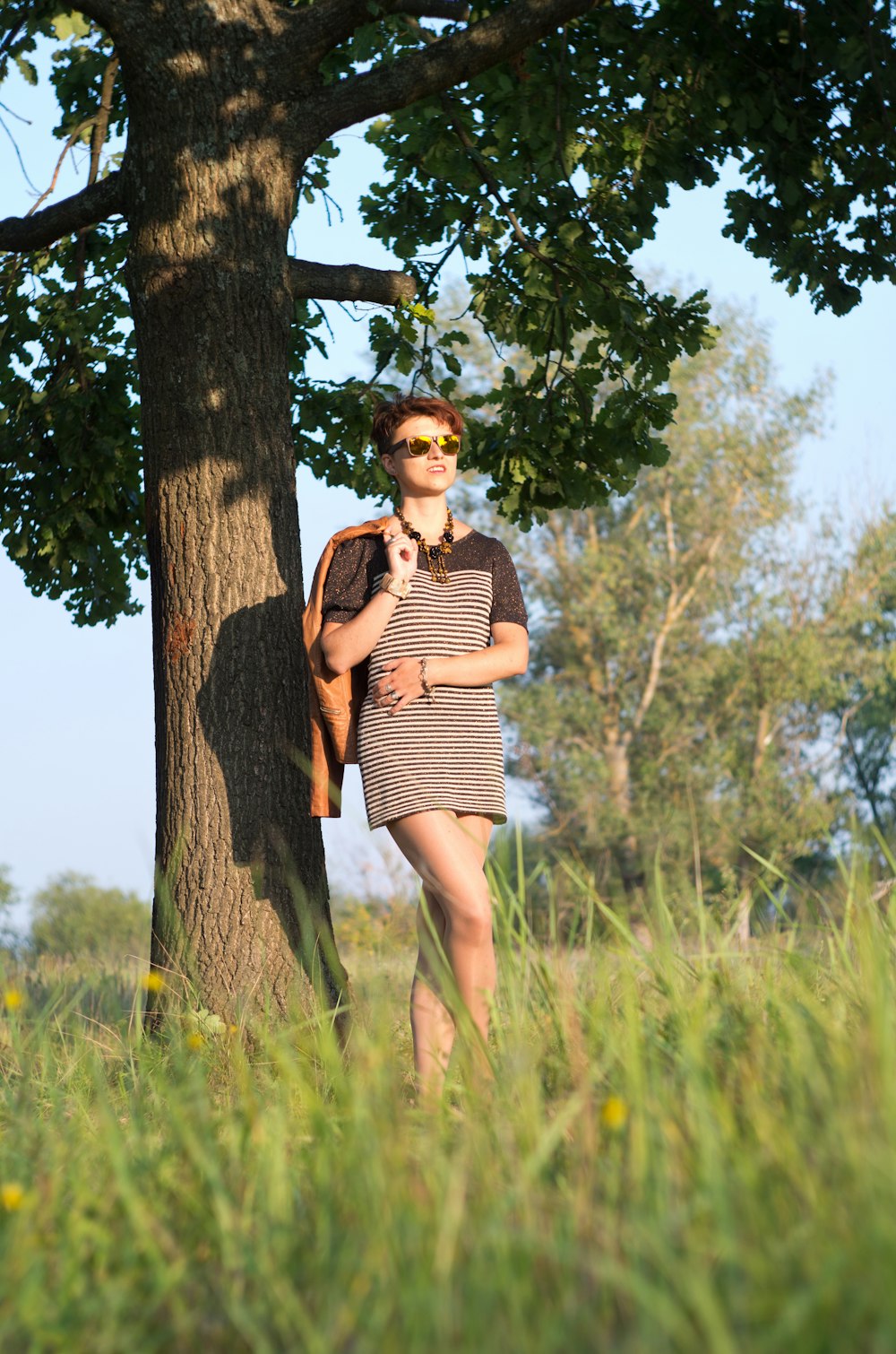 a woman standing next to a tree in a field