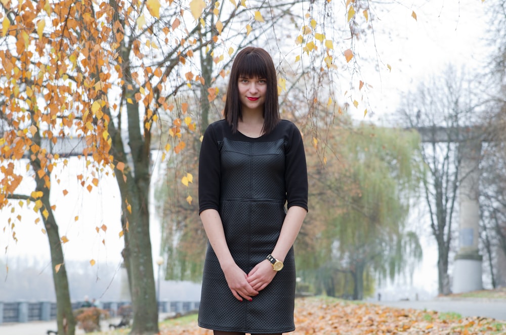a woman in a black dress standing in a park