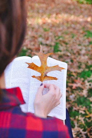 a smiling customer holding a book and sitting outdoors with vibrant autumn leaves around