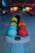 A set of colorful bowling balls is neatly arranged on a bowling ball rack, with lanes and pinsetters visible in the background. The scene is dimly lit with multi-colored lights creating a lively atmosphere.