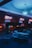A dimly lit bowling alley with glowing neon lights illuminating the area. Bowling lanes extend toward the back, accompanied by a series of scoreboards hanging from the ceiling. Several colorful bowling balls are placed in racks beside chairs and tables designed for seating near the lanes.