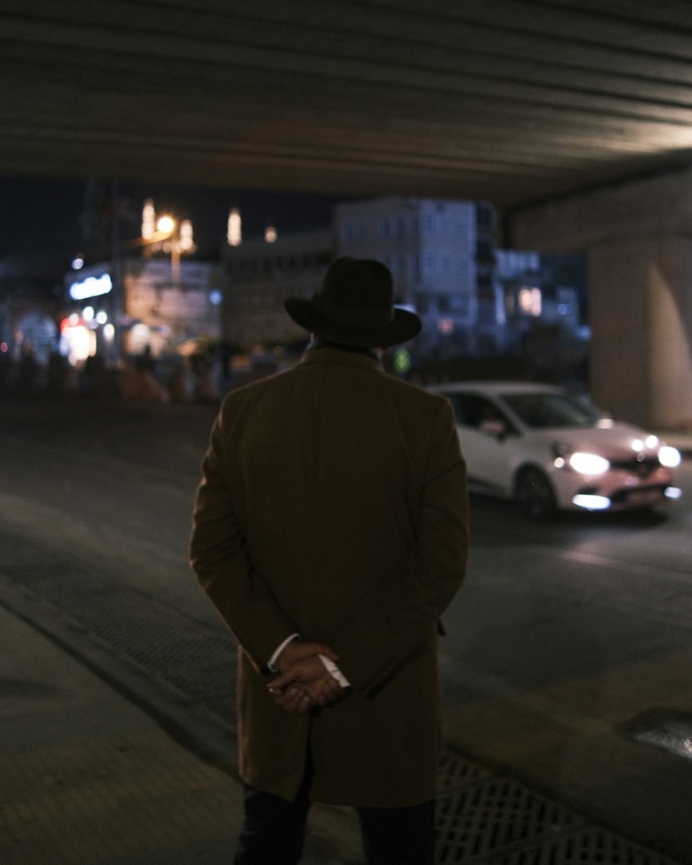 a man in a brown coat and hat standing on a sidewalk