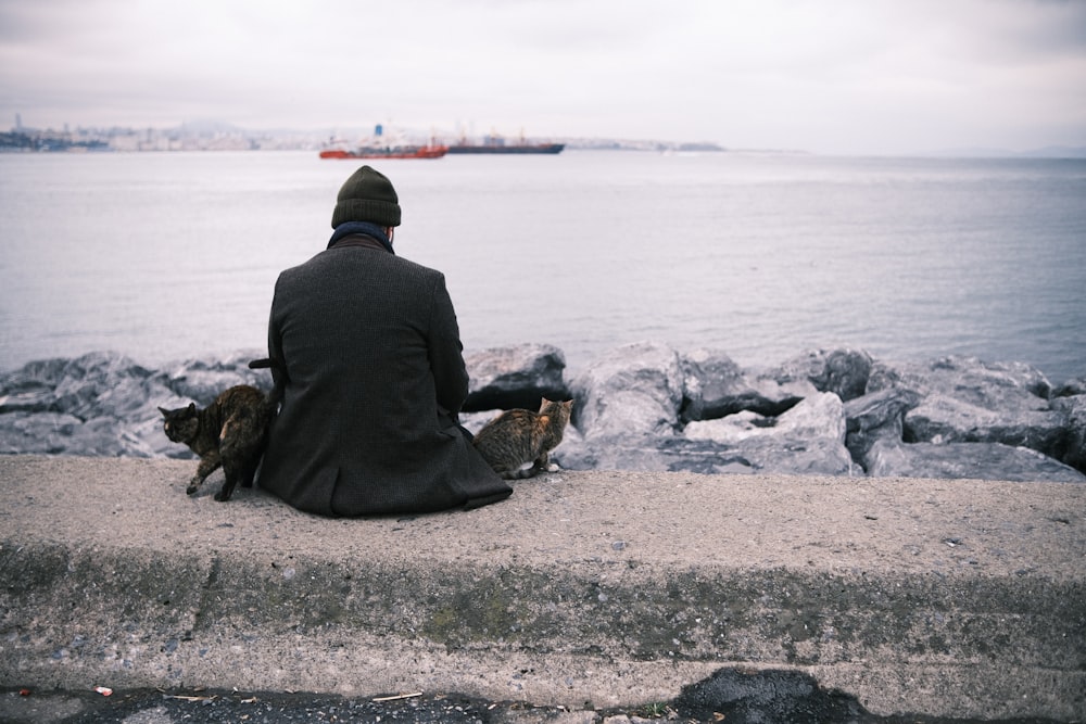 a man sitting on a ledge next to a body of water