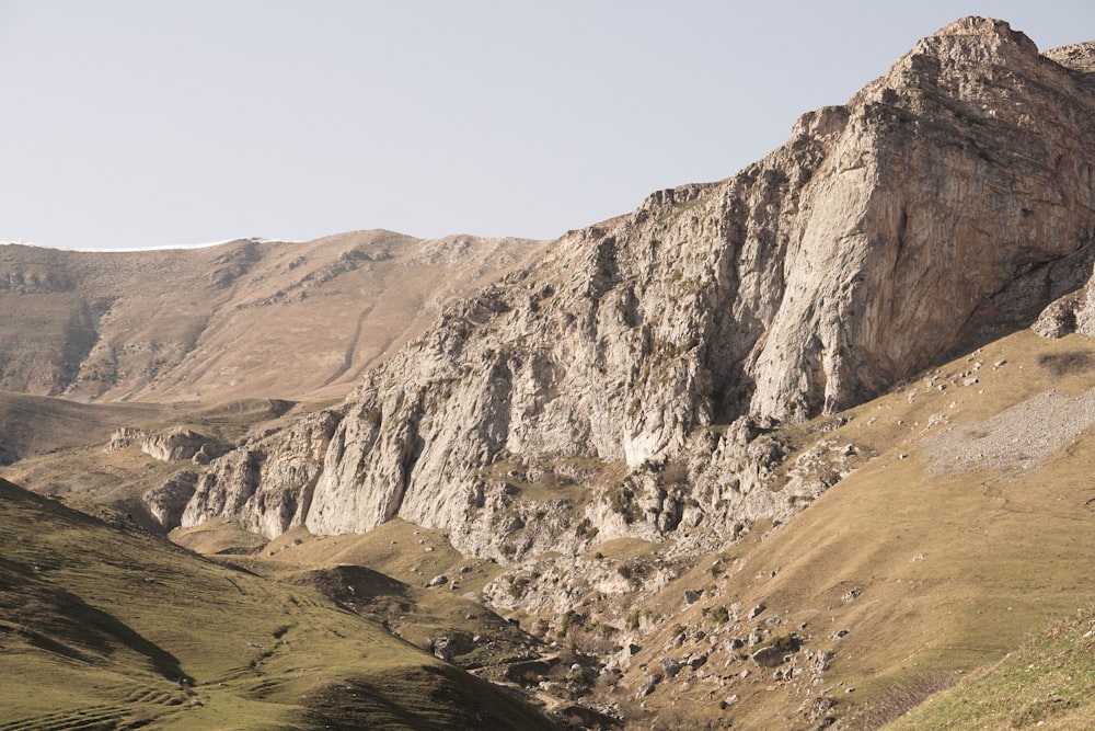 a rocky mountain with a grassy valley below