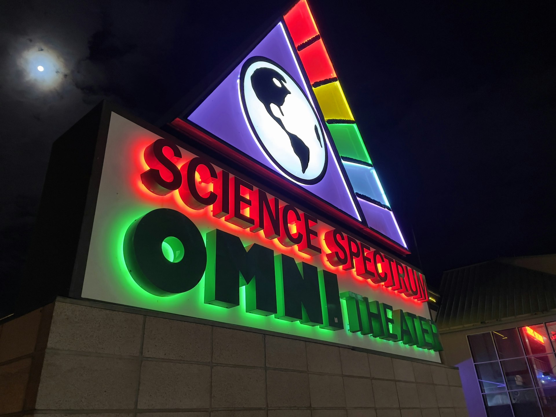 a building with a neon sign and a clock tower in the background