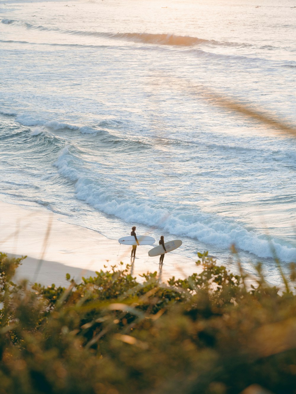 two people holding surfboards on a beach next to the ocean