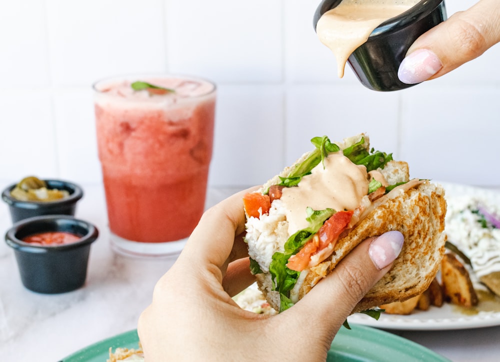 une personne versant de la vinaigrette sur un sandwich sur une assiette