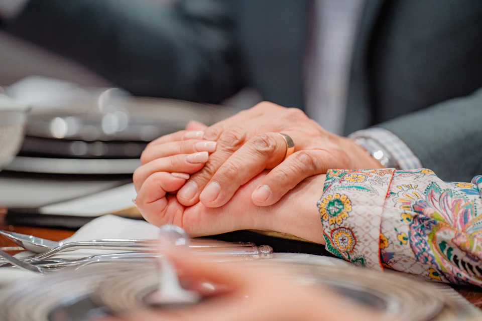 Two people hold hands on a table set for two with dinner plates