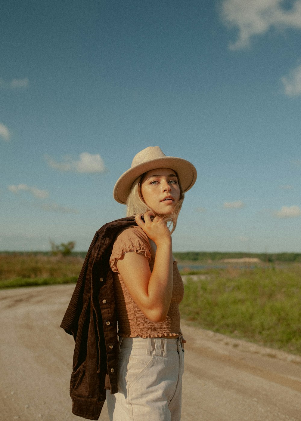 a woman in a hat is standing on a dirt road