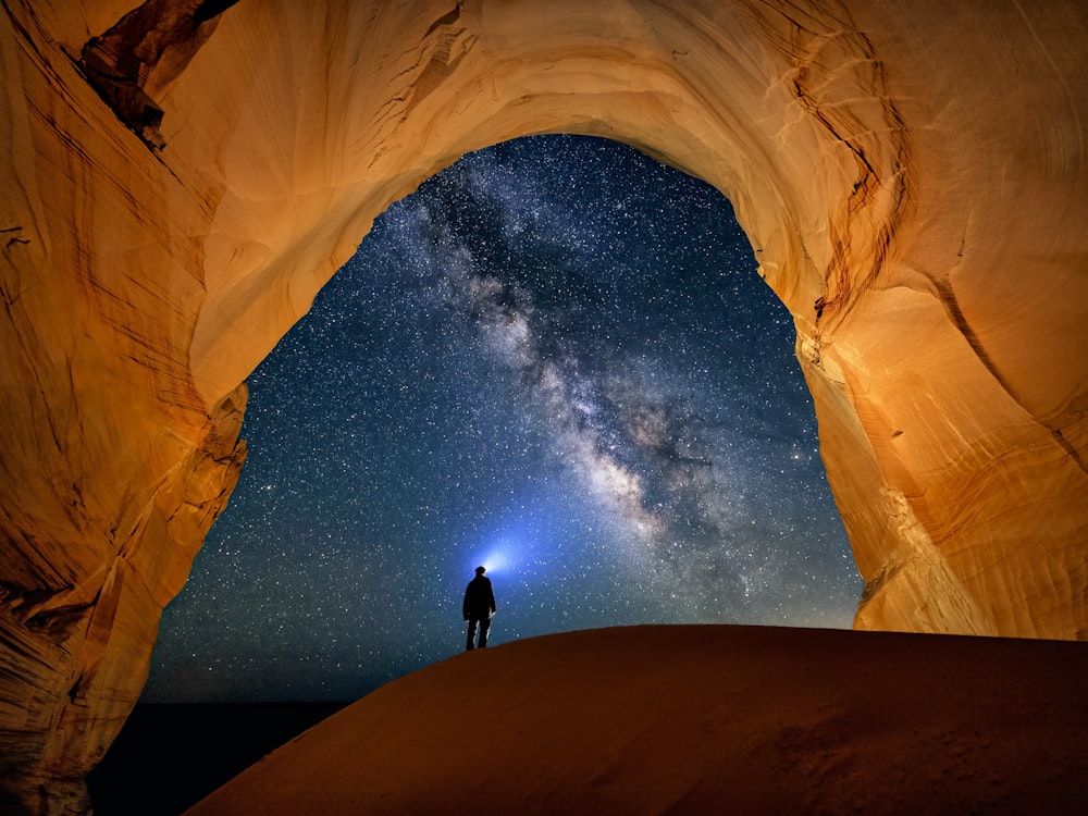 a man standing in the middle of a desert under a star filled sky