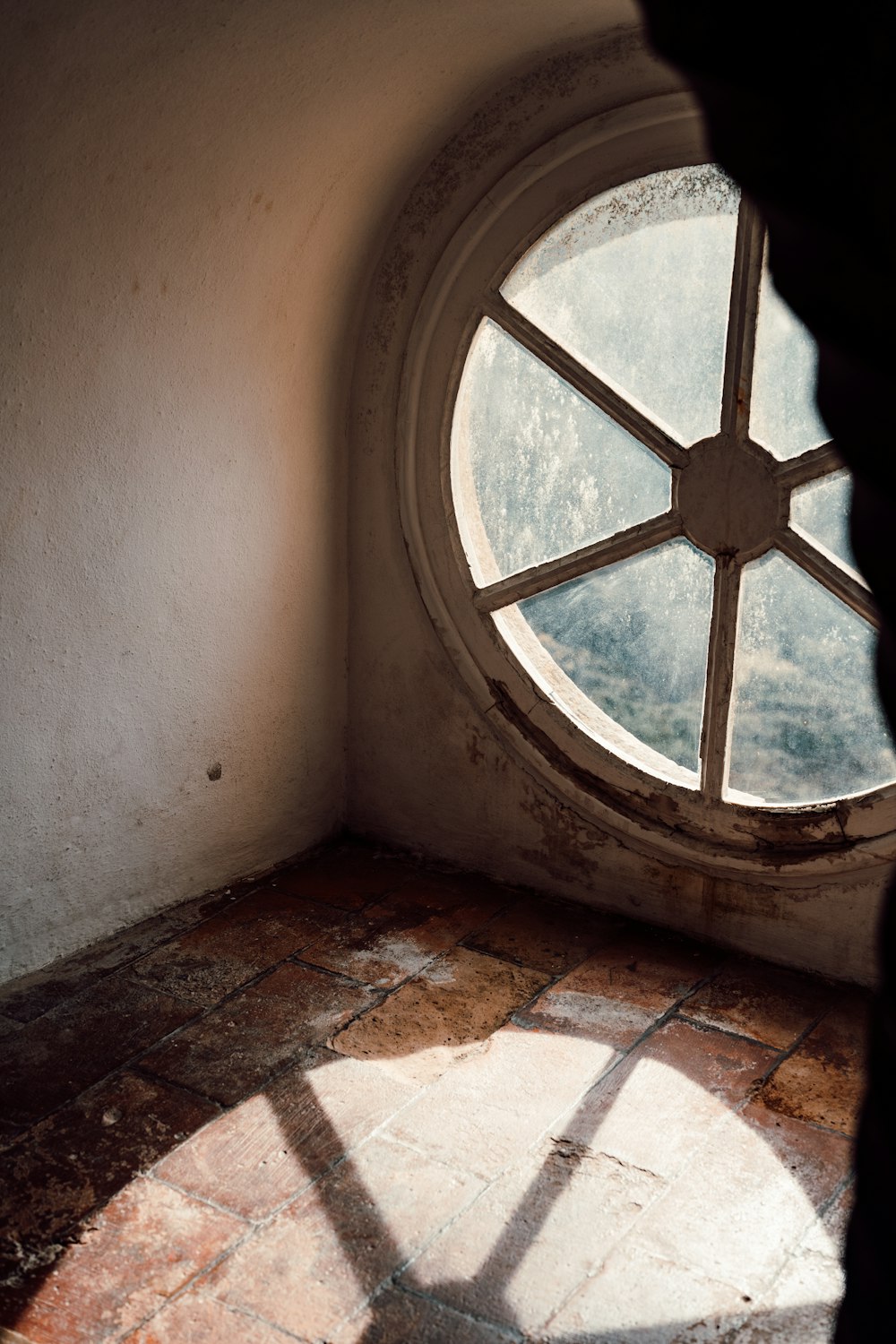 a round window in a white wall with a stone floor