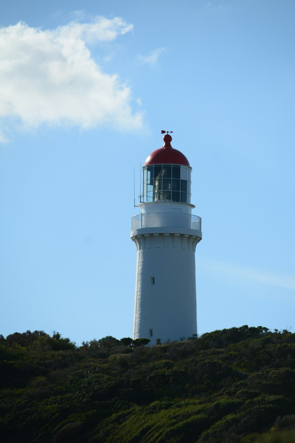a white lighthouse with a red top on a hill