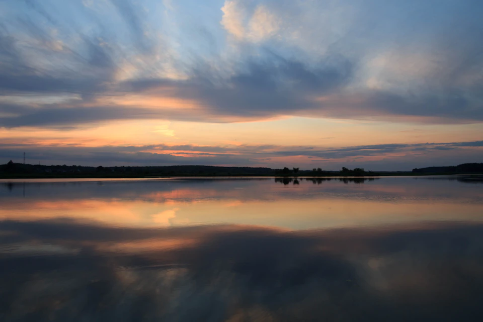 Serene lake at sunset with vibrant orange and blue hues reflected in calm water
