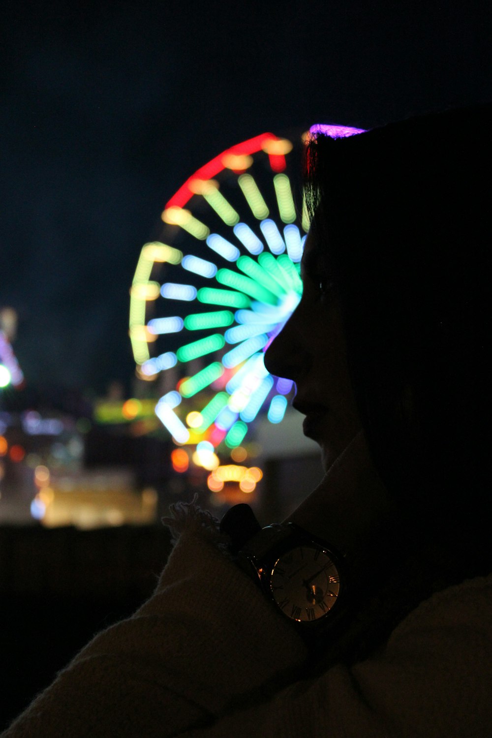 a person standing in front of a ferris wheel at night