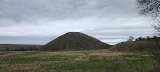 An ancient burial mound nestled in a peaceful forest setting under a clear blue sky.