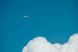 A sleek airplane soaring above fluffy white clouds against a bright blue sky.