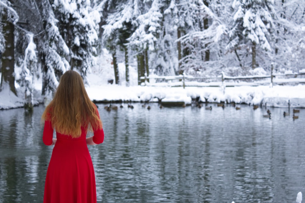 a woman in a red dress standing in front of a lake
