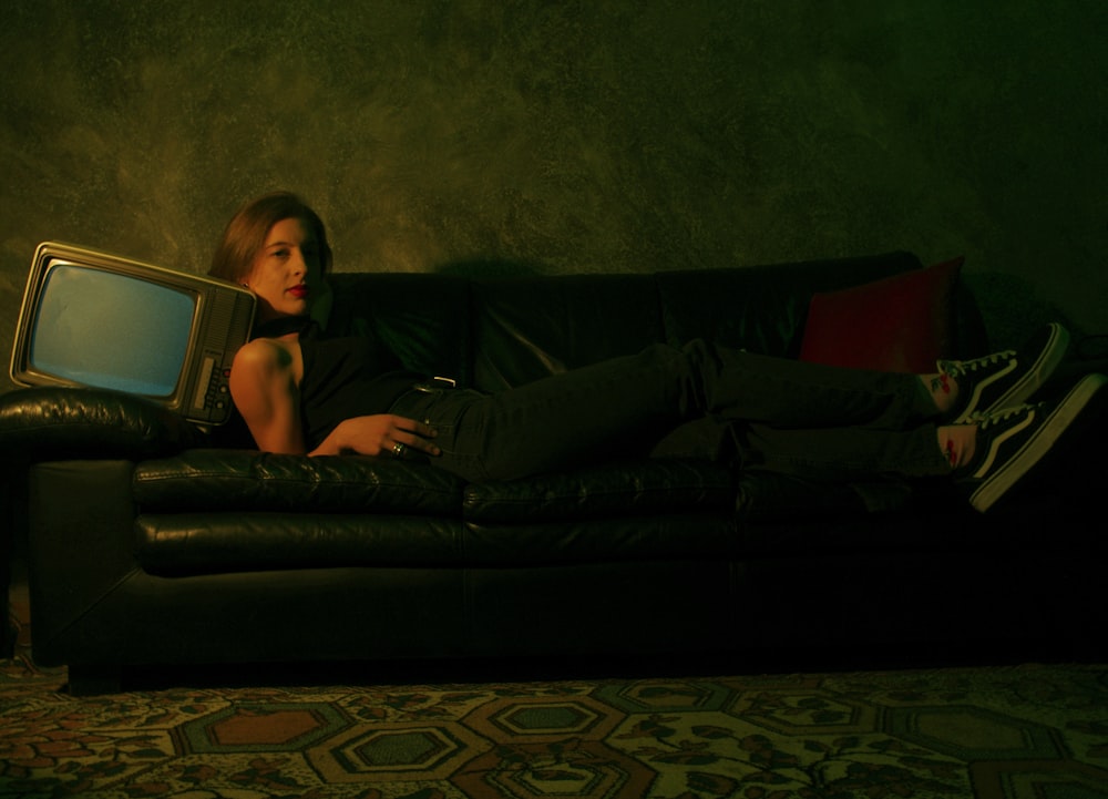 a woman laying on a couch with a television on it