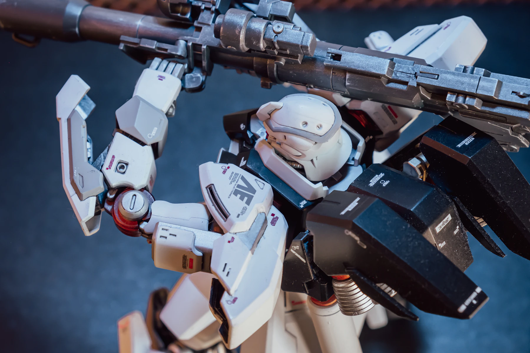 Close-up of a white and black robot model shouldering a long gray rifle