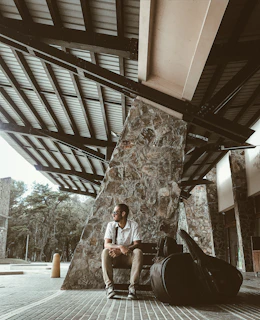 A serene outdoor shot of Steven Buitinga sitting on a bench with his guitar, surrounded by nature.