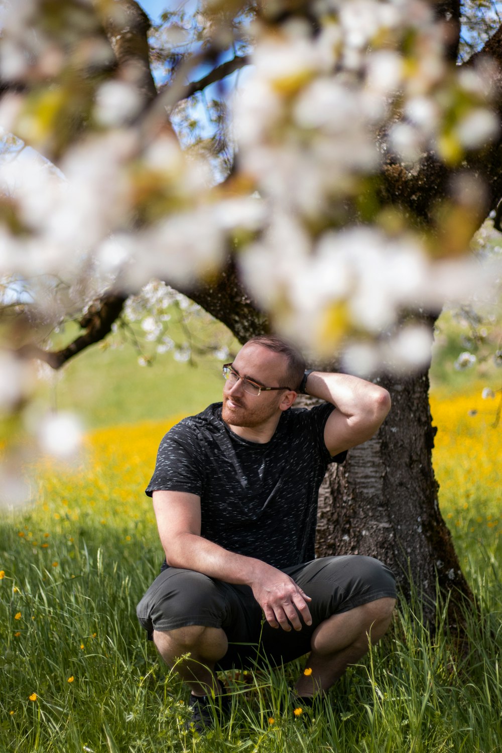 a man sitting in the grass next to a tree