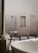 A minimalist bathroom featuring a large white marble bathtub in the foreground. The walls are tiled in a light gray stone, complemented by black fixtures including a faucet and showerheads. There is a wooden stool with rolled white towels placed on top, and small bottles are nestled in a recessed wall shelf. The floor is a mix of large square tiles and dark pebbles, adding to the spa-like ambiance.