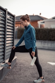 A male athlete stretching outdoors at sunrise, wearing casual workout gear and holding a supplement bottle.