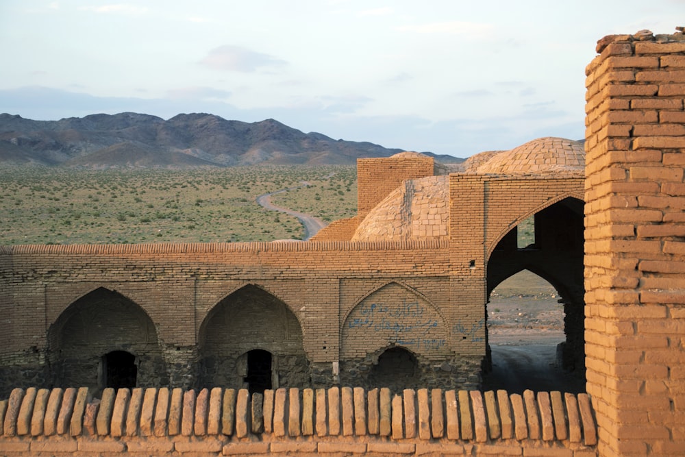 a brick building with arches and arches in front of a mountain range