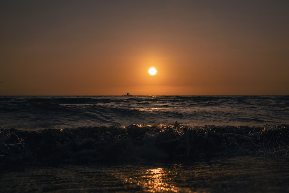 the sun is setting over the ocean with a boat in the distance