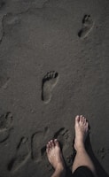 Bare feet standing on wet sand with several footprints leading away, capturing a moment by the beach or shoreline.