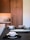 A modern kitchen or dining space featuring wooden cabinetry with clean lines. The countertop is adorned with white bowls placed on black napkins, along with a long, decorative platter. The background includes textured wall tiles and decorative vases, adding a sophisticated touch.