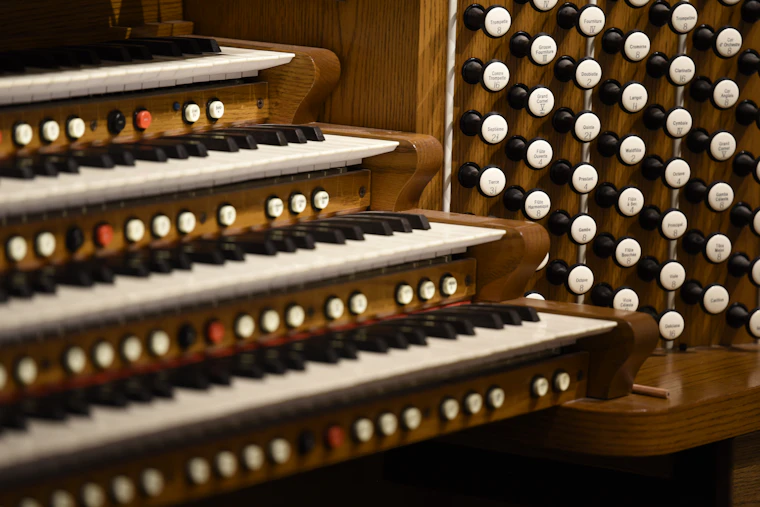Close view of an organ console with three keyboards and rows of round stop knobs