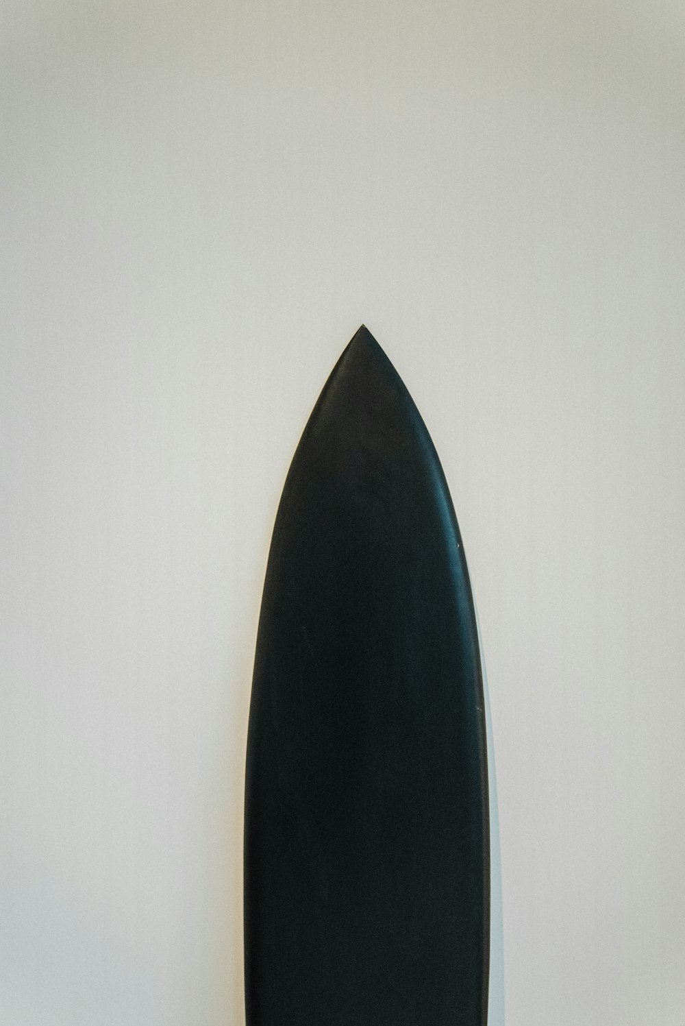 a black surfboard leaning up against a white wall