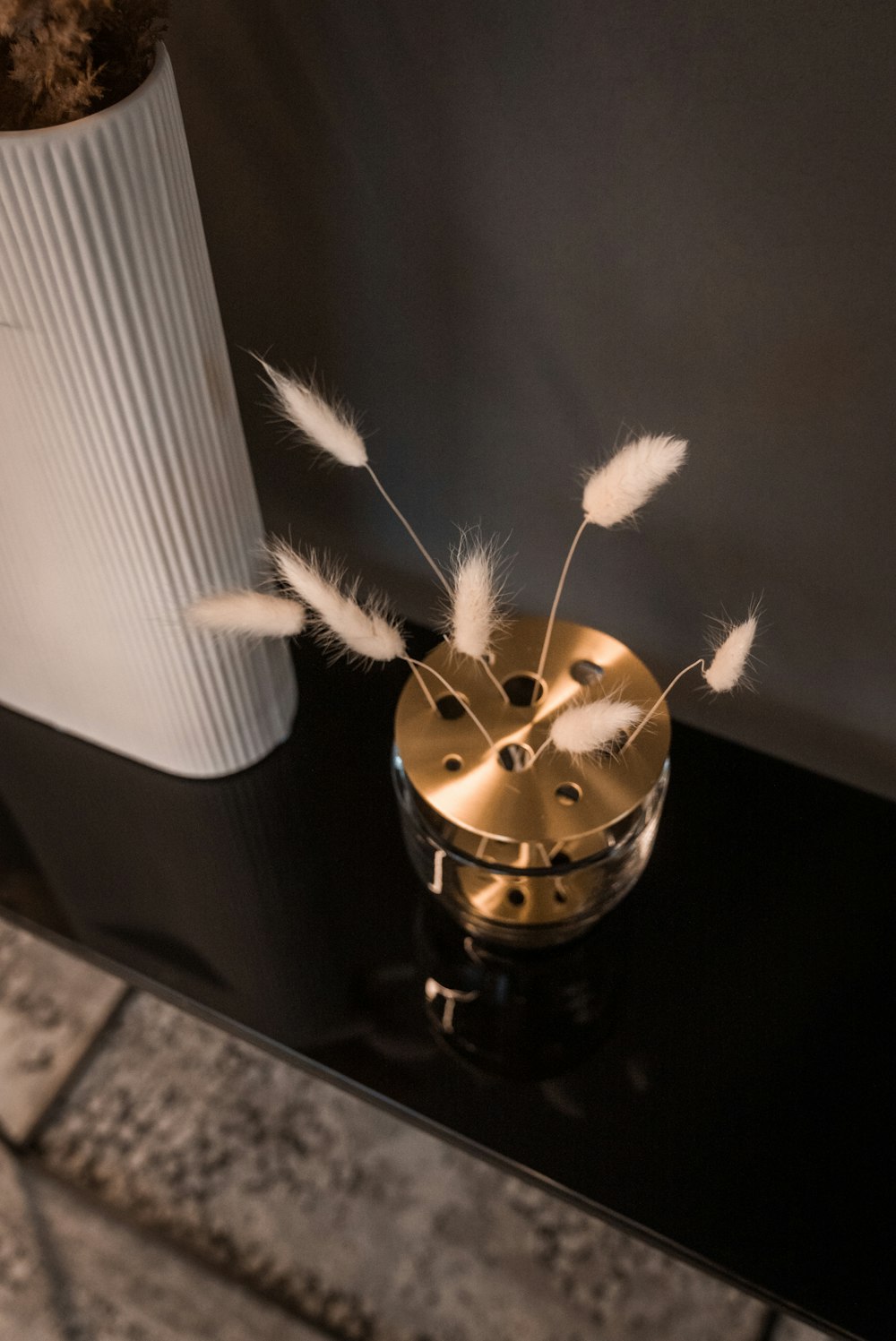 a black table with a white vase and some white feathers