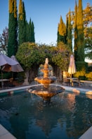 a fountain in the middle of a garden with umbrellas