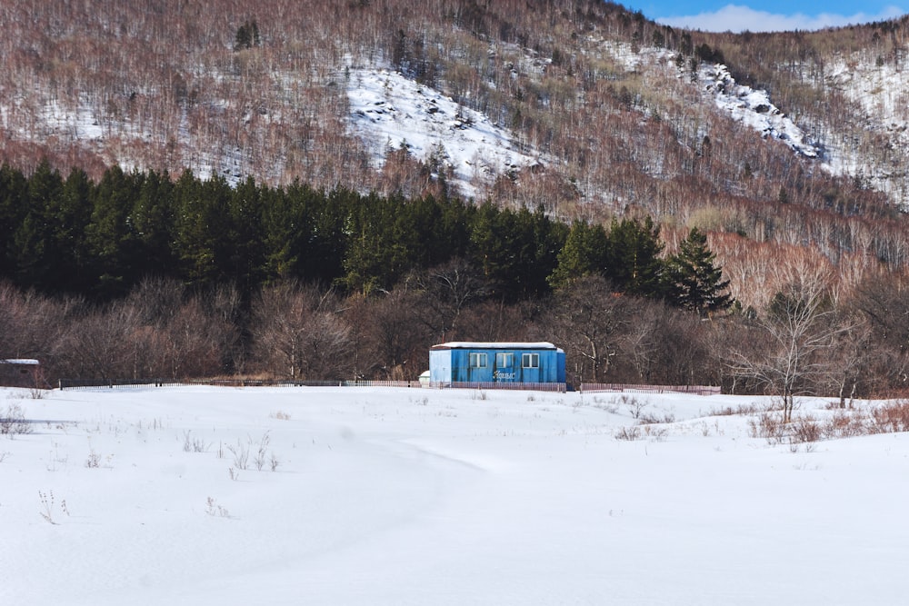 Un pequeño edificio azul sentado en medio de un campo cubierto de nieve