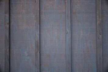 Panels of wooden siding with a weathered, aged appearance. The surface has visible grain and a slightly rough texture.