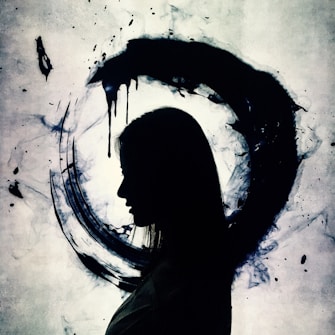 A silhouette of a person facing left, set against a textured background featuring a large, dark, circular brushstroke along with ink splatters. The contrast between the black silhouette and lighter shades of blue and gray in the background creates a striking visual effect.