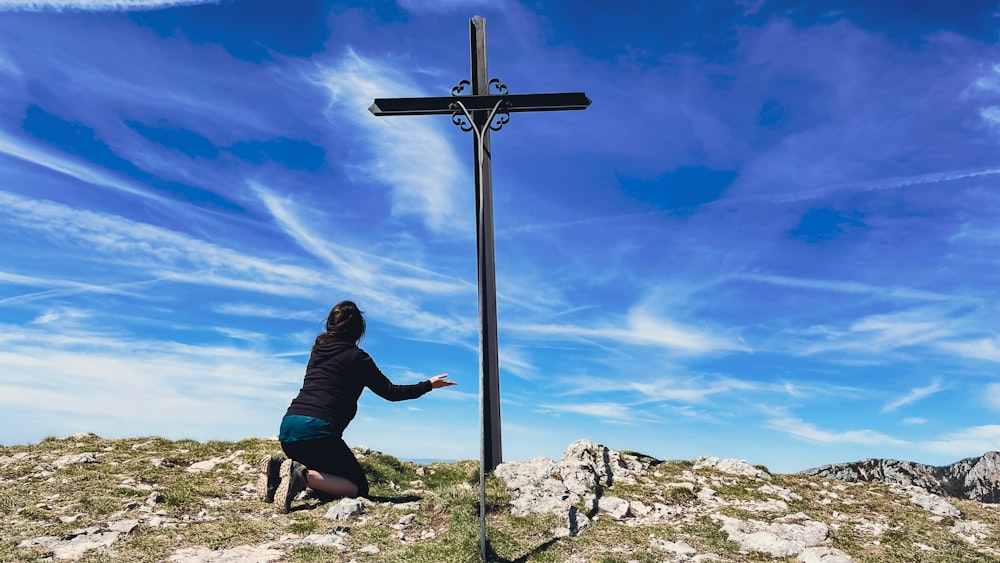 a woman kneeling down next to a cross on top of a hill