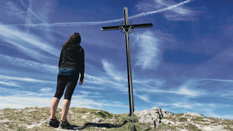 a woman standing next to a cross on top of a hill