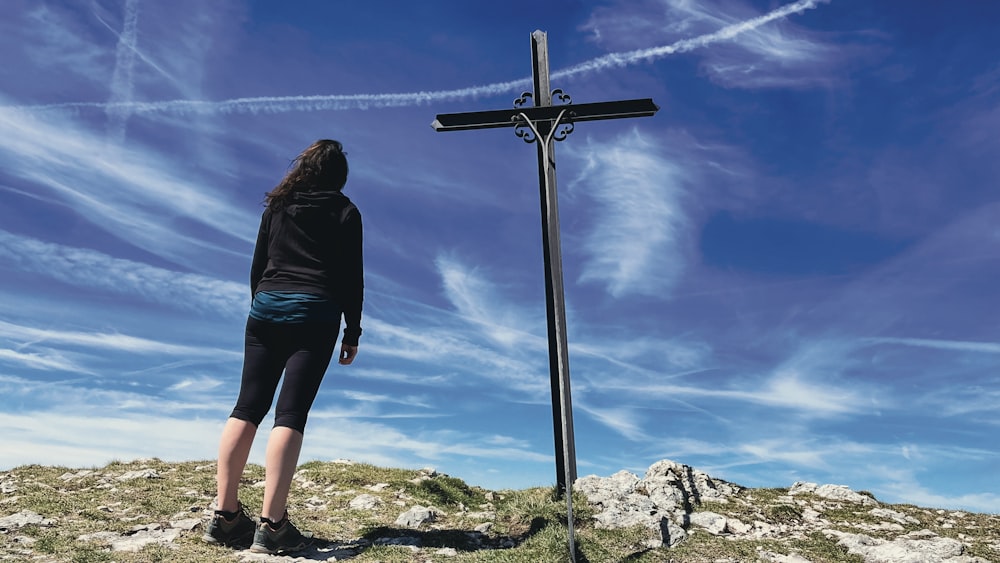 a woman standing next to a cross on top of a hill