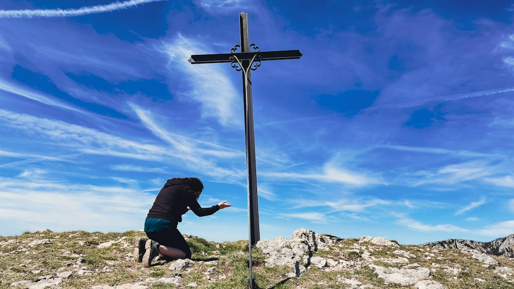 a man kneeling down next to a cross on top of a hill