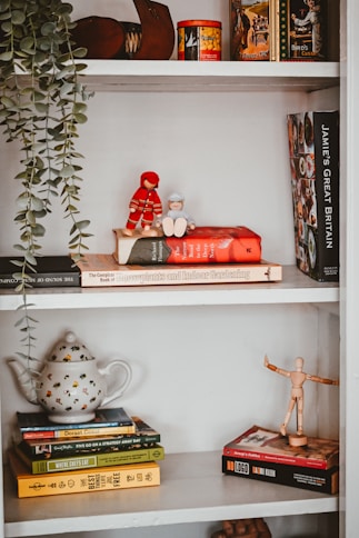 a white book shelf with books and a red teddy bear