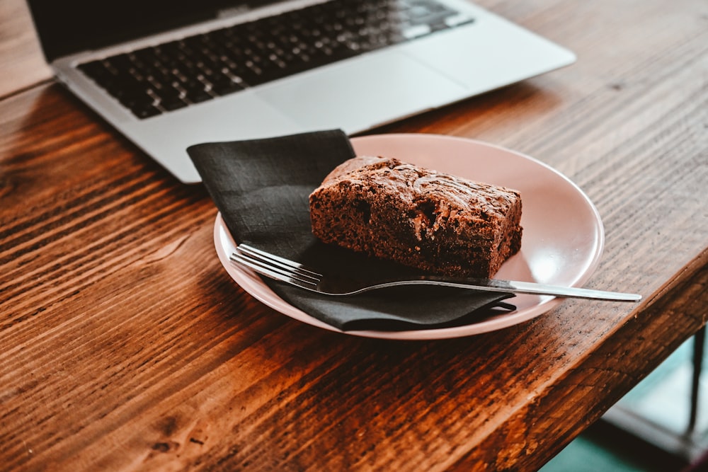 a plate with a piece of cake on it next to a laptop